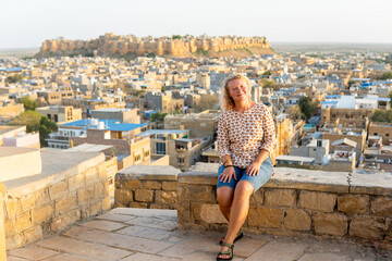 Young blonde European woman travelling in Rajasthan, enjoying panoramic view of Jaisalmer city fort, India