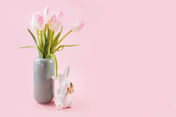 Beautiful pink tulips in vase and white Easter bunny figurine on pastel pink background. Happy easter greeting or invitation card. Copy space for text