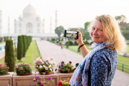 Attractive young woman taking photos of the iconic marble white Taj Mahal mausoleum in Agra, Uttar Pradesh, India