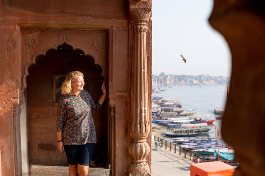 Blonde woman exploring the waterfront of Varanasi ancient town. Enjoying the sunny day on the Ganges river promenade, India