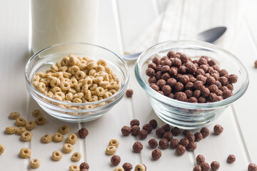 Breakfast cereal rings and chocolate balls in bowl on white table.