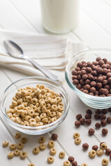 Breakfast cereal rings and chocolate balls in bowl on white table.