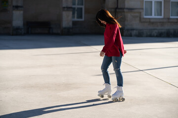Fototapeta premium Young woman roller skating downtown, wearing red sweater and jeans, enjoying urban recreational moment with energetic movement