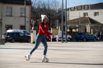 Young woman roller skating in bright red sweater, white beanie, gliding through sunlit city square, enjoying winter urban freedom with cheerful movement