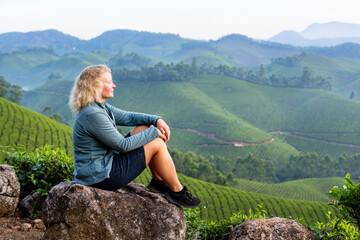 Naklejka premium Young European woman enjoying panoramic view over tea plantations in Munnar, Kerala, India