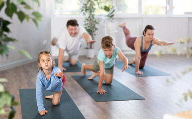 Pleasant little girl practicing table pose one hand and one leg raised together with her family...