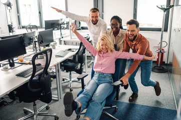 Business colleagues pushing businesswoman on office chair, having fun at work