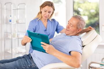 Obraz premium Old man patient discussing documents regarding treatment procedures with middle-aged doctor
