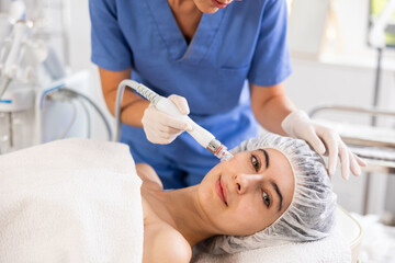 Young female patient undergoing device-driven facial treatment using ion bubble pen attachment for...