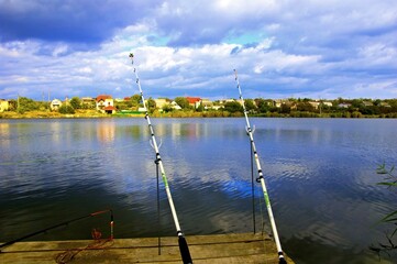 Two fishing poles are leaning against a dock in front of a lake