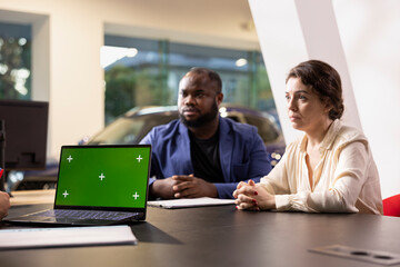 Salesman showing car features on green screen laptop to customers, hoping to close deal. Showroom agent trying to persuade clients to make purchase by presenting vehicle addons on mockup notebook