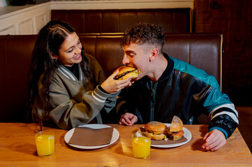 Happy couple eating burgers and drinking orange juice in a burger restaurant