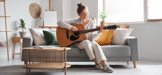 Young woman playing guitar on sofa in living room
