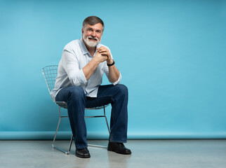 Portrait of a casual senior sitting on a chair on blue background