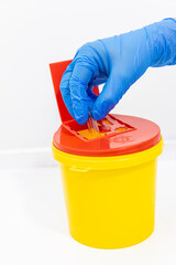 Old medicine syringes thrown into a medical waste container. The syringe is placed in the medical waste bin. A red-lidded hazardous material bin. Needles being put ito a sharps bin.