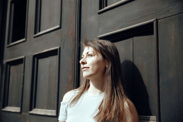 Fototapeta premium Thoughtful woman standing by a rustic wooden door under natural sunlight