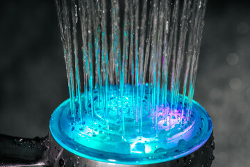 Vibrant LED shower head emitting flowing water streams with glowing blue and purple hues, showcasing a modern, colorful design. Droplets add texture and depth.