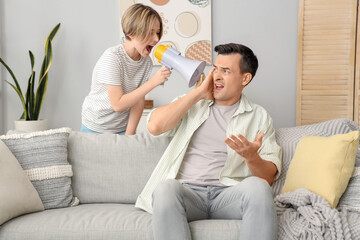 Young man stressed of his noisy little son with megaphone at home