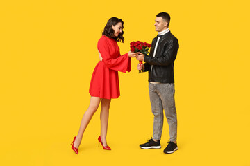 Beautiful young woman receiving bouquet of beautiful roses from her boyfriend on yellow background. Celebration of Saint Valentine's Day