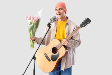Male artist with tulips and guitar singing on light background. International Women's Day celebration