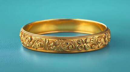 A gold band with intricate carvings placed on a vibrant teal background with subtle reflections.