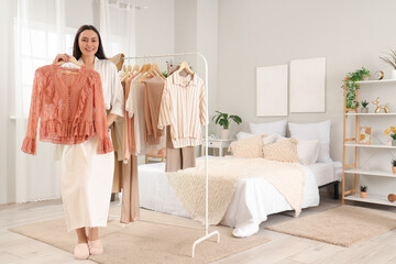 Young woman with stylish blouse near clothes rack in bedroom
