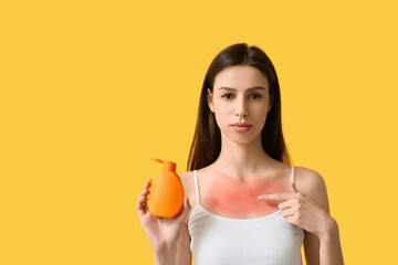 Young woman with red sunburned skin pointing at bottle of cream on yellow background