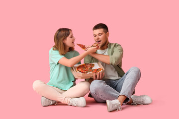Beautiful young shocked couple with cardboard box of tasty pizza sitting on pink background