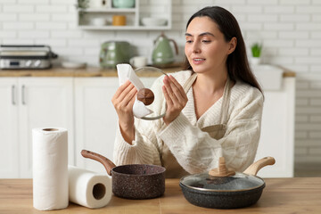 Beautiful young happy woman wiping pots with paper towels in kitchen