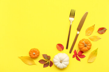 Stylish cutlery with fresh pumpkins and autumn leaves on yellow background