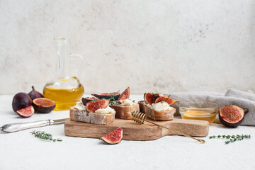 Wooden board of delicious fig bruschetta with ricotta cheese and rosemary on white background