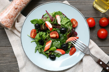 Plate of salad with crab sticks, spinach, black olives and tomatoes on wooden background