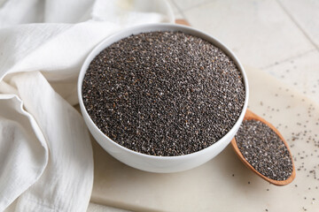 Bowl and wooden spoon with chia seeds on white tile background
