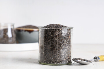 Jar and spoon with chia seeds on white background