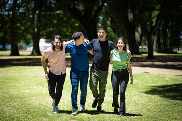 Group of latin friends walking arm in arm in a park under a bright sun