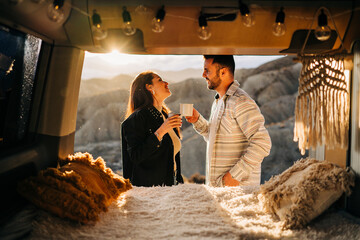 Couple enjoying coffee inside camper van at sunset in desert landscape