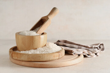 Wooden tray and bowl of raw rice with scoop on light background