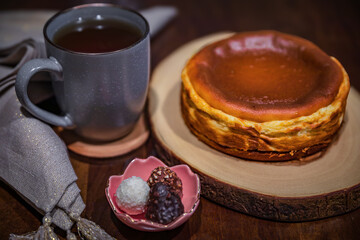 Basque cheesecake with a cup of tea and a few chocolates on a dark wooden table