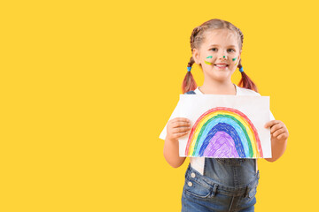 Little girl in paint with drawn rainbow on yellow background