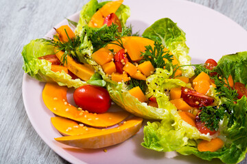 Salad with baked pumpkin. Lettuce, pumpkin, cherry tomatoes, sesame put on a plate. Season with olive oil sauce, salt, pepper, lemon and pumpkin puree.