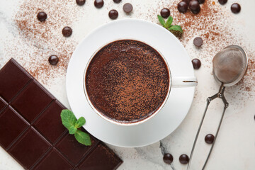 Cup of hot chocolate with cocoa powder, chips and strainer on marble background