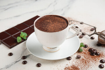 Cup of hot chocolate with cocoa powder, chips and strainer on marble background