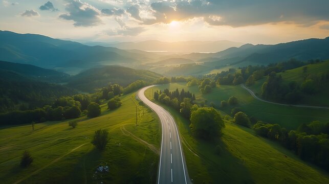 Aerial view of road in green meadows at summer sunny day. Top view from drone of rural road, mountains, forest. Beautiful landscape with roadway, sun rays, trees, hills, green grass, clouds. Slovenia