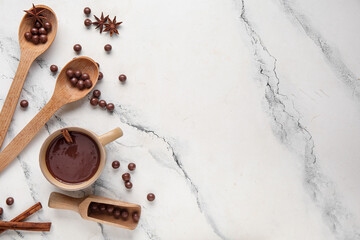 Cup of hot chocolate with wooden spoons, balls and cinnamon sticks on marble background