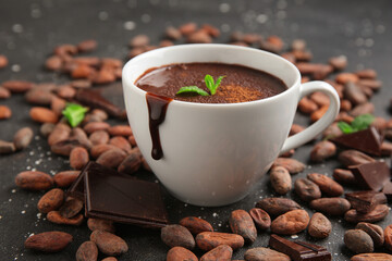 Cup of hot chocolate with mint leaves and cocoa beans on black grunge background