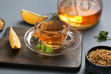 Glass cup of hot buckwheat tea with lemon slice and mint leaves on grey background
