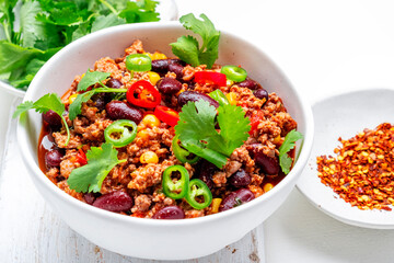 Chili con carne with minced beef, beans, paprika, corn, cilantro, jalapeno pepper in tomato sauce, white background, top view