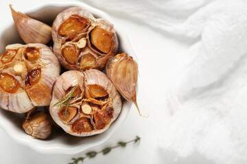 Bowl with baked garlic on white background