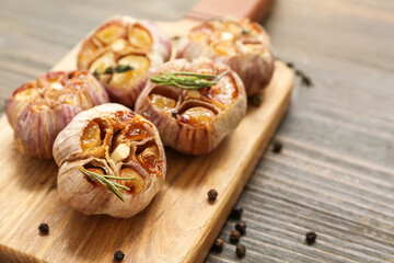 Board with baked garlic, peppercorns and rosemary on wooden background