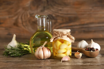 Jug and jar of fresh garlic oil with peppercorns on wooden background